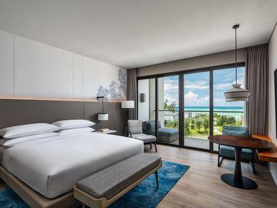 Chambre d'hôtel moderne avec grand lit, bureau et balcon avec vue sur la mer.