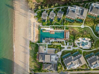Vue aérienne d'une station avec plusieurs bâtiments, une piscine et une plage de sable au bord de l'eau.