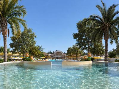 Grande piscina limpida circondata da palme e giardino verde sotto un cielo azzurro.