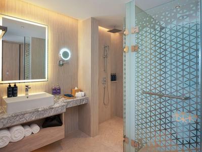 Bagno moderno in hotel con specchio illuminato, doccia in vetro e asciugamani sul piano in marmo.