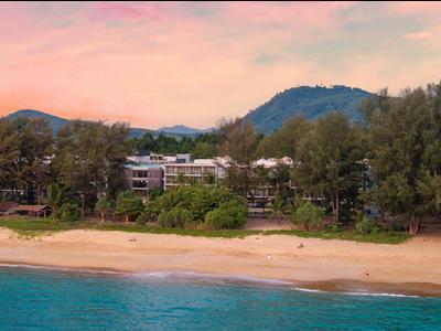 Spiaggia con acqua turchese, alberi e hotel sullo sfondo al tramonto.