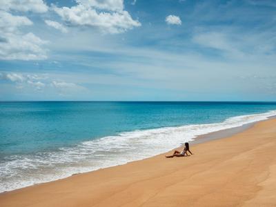 Ampia spiaggia sabbiosa con una persona sola e mare blu calmo sotto un cielo nuvoloso.