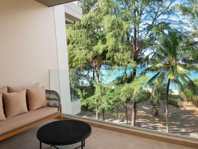 Balcone con divano e tavolo, vista su alberi verdi e cielo azzurro, atmosfera da hotel.