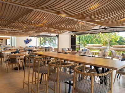 Ristorante dell'hotel luminoso con lunghi tavoli in legno, sedie e vista su piante tropicali.