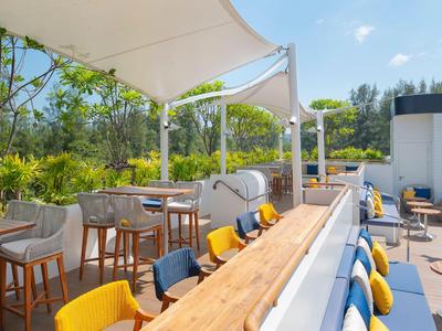 Terrazza soleggiata dell'hotel con sedie colorate, tavoli in legno e tende bianche.