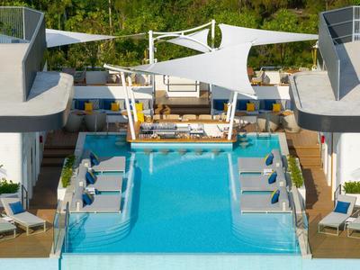 Piscina moderna dell'hotel con lettini e vele bianche, circondata da verde.