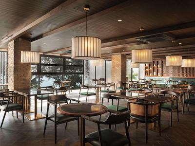 Ristorante di un hotel moderno con mobili in legno, grandi finestre e illuminazione soffusa.