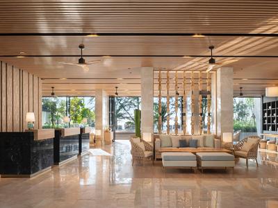 Lobby di hotel moderna con soffitto in legno, pavimento in marmo e aree salotto con vista su spazio verde esterno.
