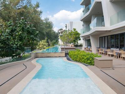 Piscina moderna dell'hotel con posti a sedere e vegetazione circostante alla luce del giorno.