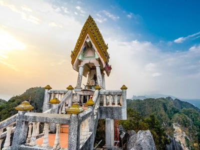 Tempel mit Treppe auf Berggipfel, umgeben von Bergen und blauem Himmel bei Sonnenuntergang.