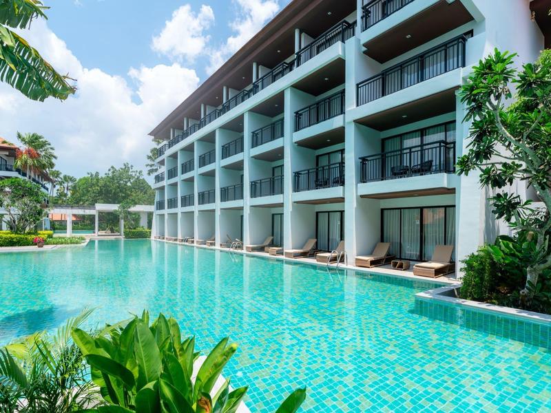 Moderne hotelzwembad met helder water en ligstoelen bij een meerlaagse gebouw.