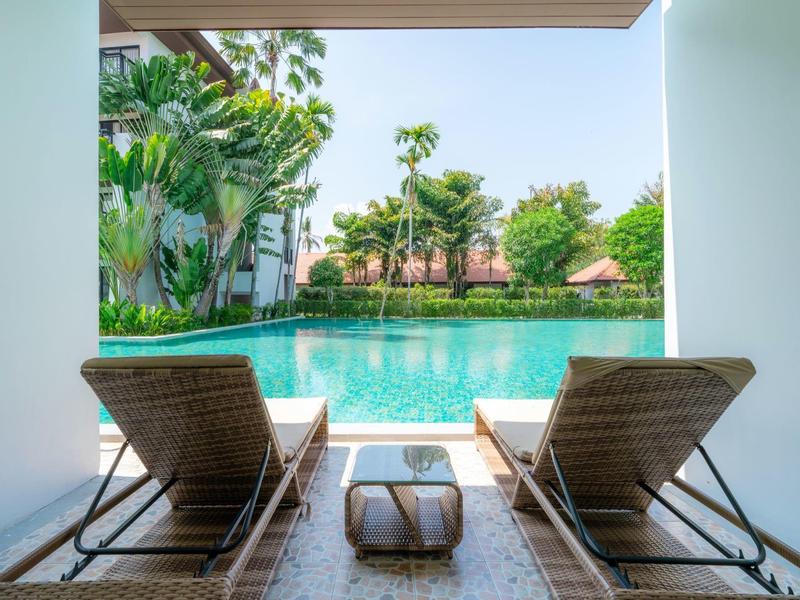 Uitzicht vanaf een overdekt terras met twee ligstoelen op een zwembad en groene tuin.