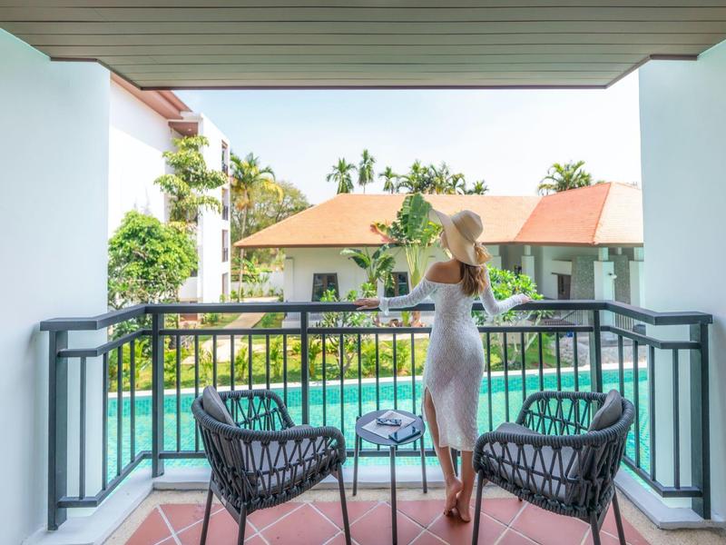 Vrouw op balkon met stoelen en tafel, uitzicht op zwembad en tropische vegetatie.