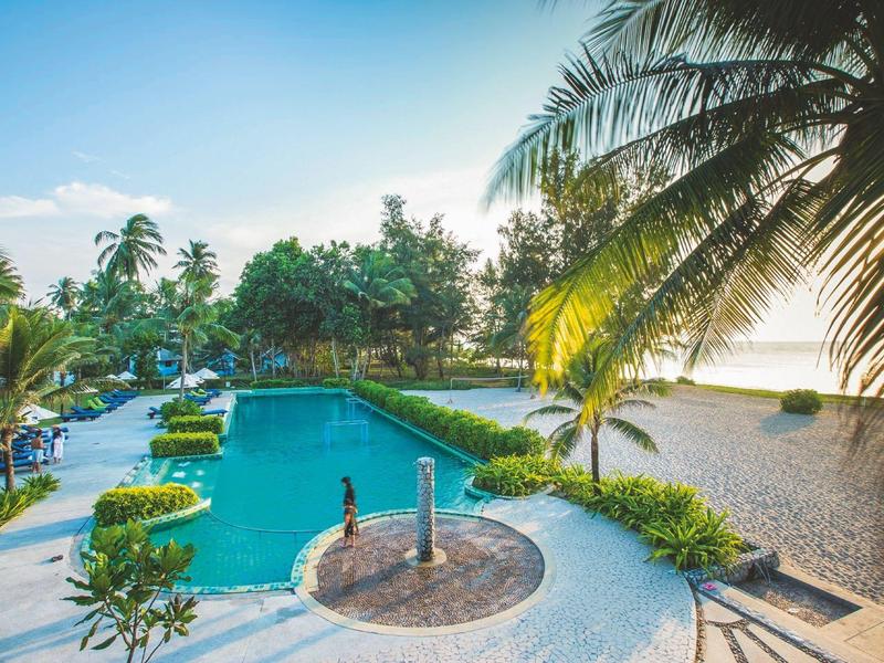 Zwembad met palmbomen en uitzicht op het strand bij zonsondergang.