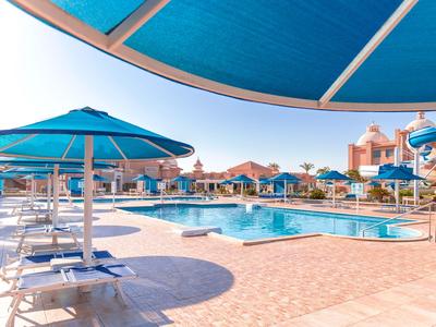Poolbereich eines Hotels mit blauen Sonnenschirmen und Liegestühlen unter klarem Himmel.
