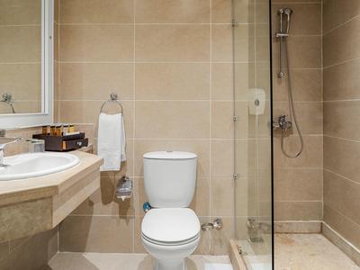 Kompaktes Badezimmer mit weißer Toilette, eckigem Waschbecken, Duschecke und hellbeigen Fliesen.