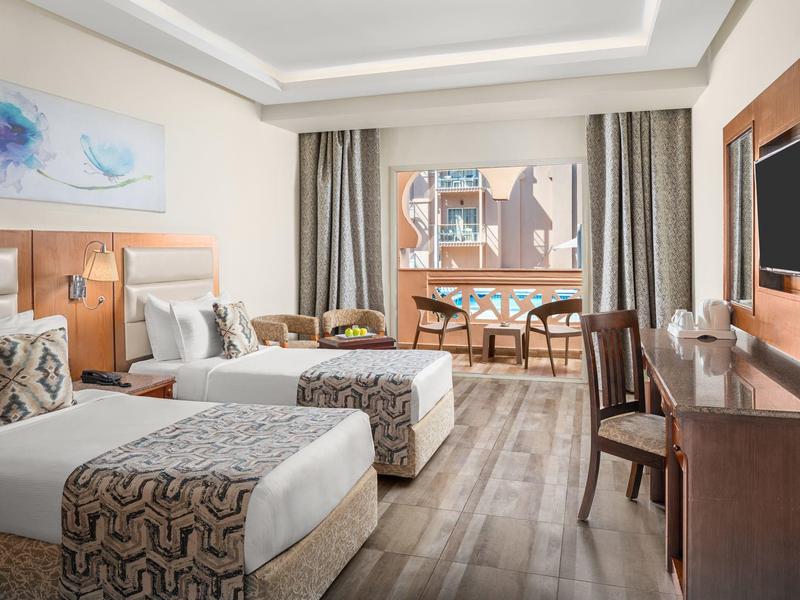 Helles Hotelzimmer mit zwei Betten, Holzboden, Schreibtisch, Stühlen und großer Fensterfront.