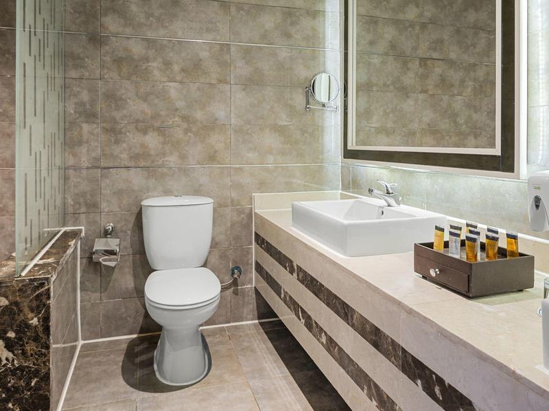 Modernes Badezimmer mit weißer Toilette, eckigem Waschbecken, großer Spiegelfläche und beigefarbenen Fliesen.