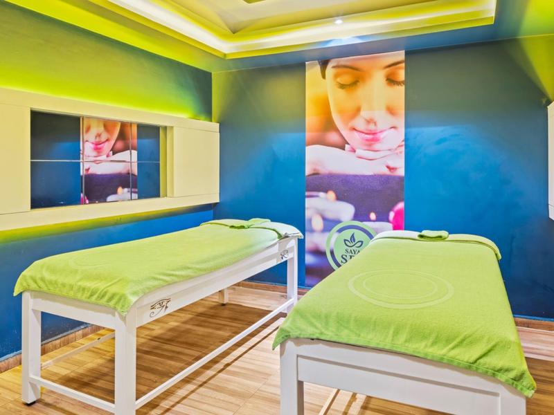 Modernes Wellnesszimmer mit zwei grünen Massageliegen, blauen Wänden und hellem Holzboden.