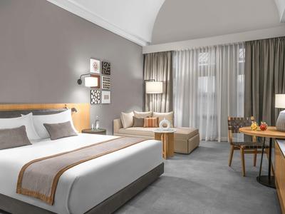 Modernes Hotelzimmer mit großem Bett, Sofa, Schreibtisch und großen Fenstern mit Vorhängen.