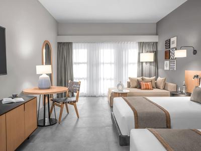 Modernes Hotelzimmer mit zwei Betten, Holzmöbeln, großem Fenster und neutralen Farbtönen.