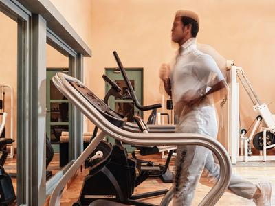 Man jogging on treadmill in a gym with various exercise machines.