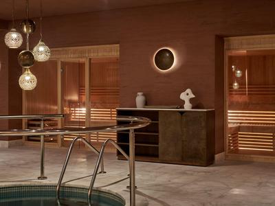 Innenraum einer Sauna mit Holzbänken und einem kleinen Pool, warm beleuchtet, in Braun- und Beigetönen.