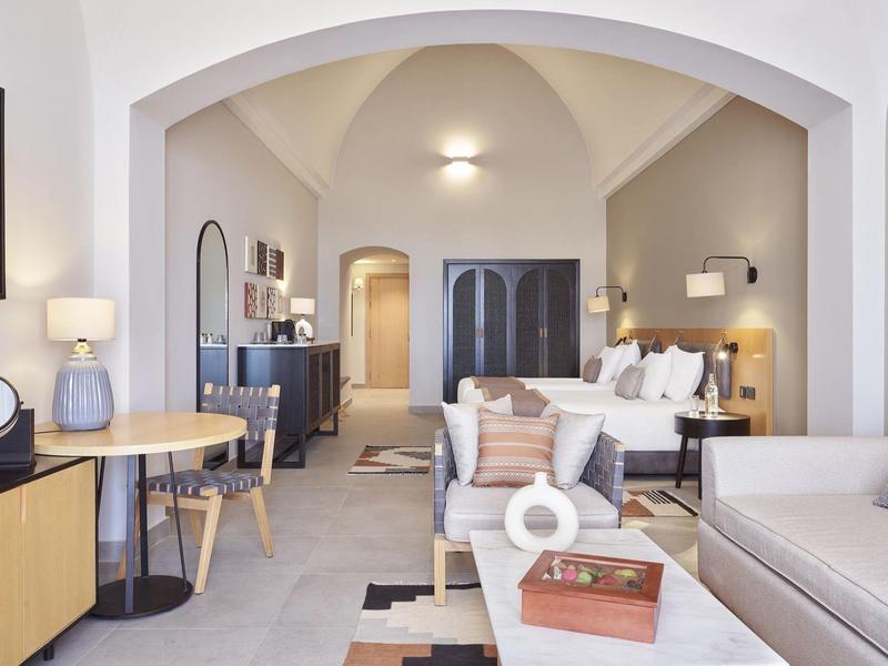 Helles, modernes Wohnzimmer mit hellgraßen Wänden, Sofa, Teppich und Holzmöbeln unter gewölbter Decke.