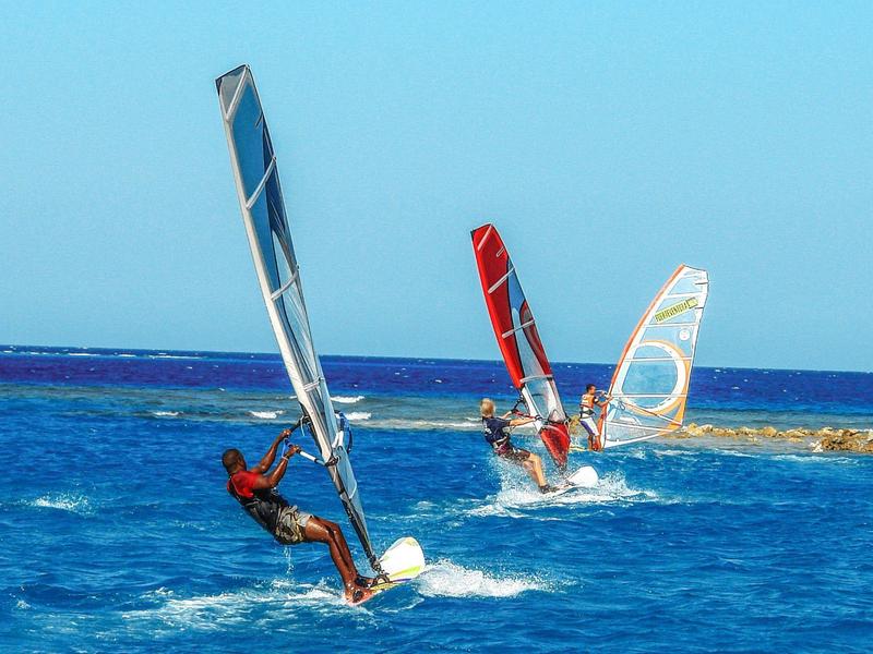 Drei Windsurfer segeln auf blauem Meer bei klarem Himmel.