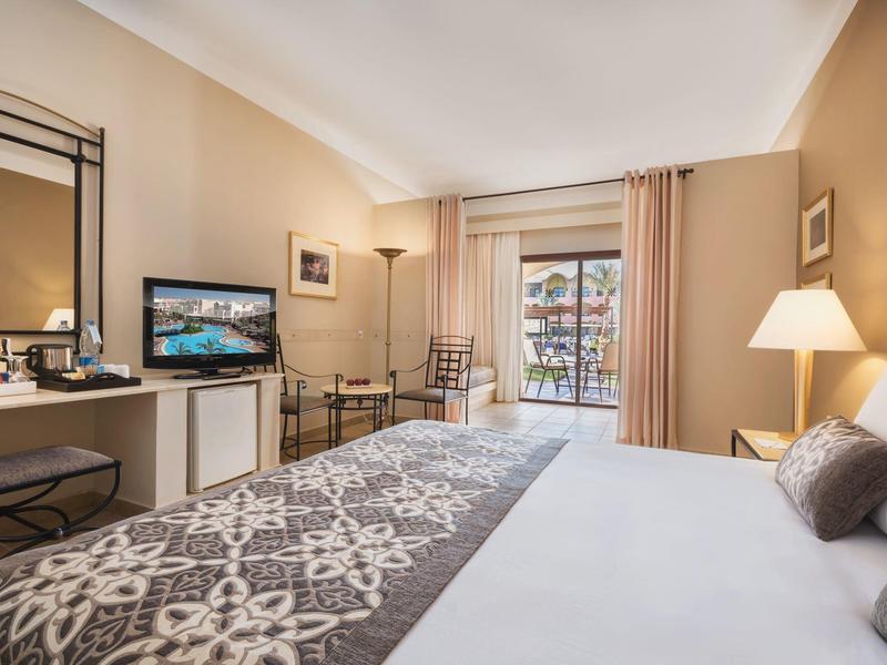 Helles Hotelzimmer mit großem Bett, Fernseher, Schreibtisch und Balkon mit Blick auf den Innenhof.