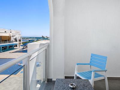 Balkon mit blauem Stuhl, Glasgeländer und Blick auf Hafen bei klarem Himmel.