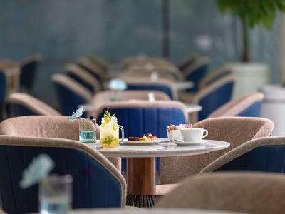 Ein runder Tisch mit Tassen, Gläsern und Blumen, umgeben von gepolsterten Stühlen in Café-Atmosphäre.