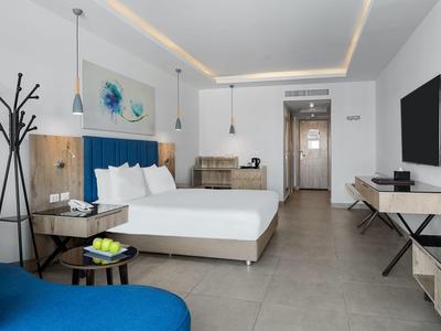 Modernes Hotelzimmer mit großem Bett, blauem Sessel, minimalistischer Einrichtung und heller Beleuchtung.