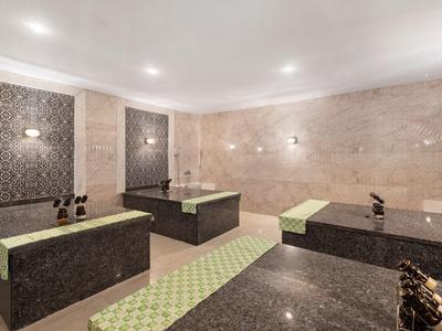 Ein heller Wellnessraum mit dunklen Marmorliegen und beige-grünem Bodenmuster.