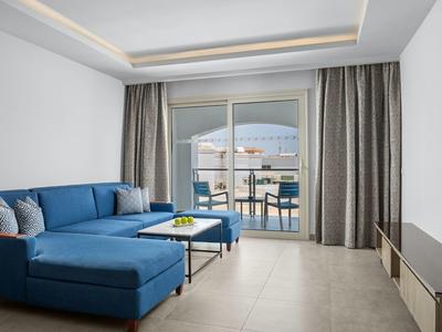 Moderner Wohnraum mit blauer Eckcouch, weißem Tisch und großer Glasschiebetür zum Balkon.