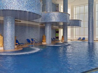 Piscina interna moderna con piastrelle a mosaico blu e aree lounge in un hotel.