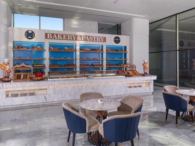 Pasticceria luminosa con vetrina in vetro e area salotto con tavoli e sedie.