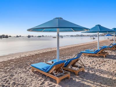 File di lettini con cuscini blu e ombrelloni su spiaggia sabbiosa vicino ad acqua calma.
