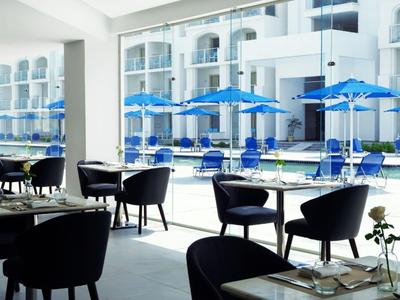 Ristorante moderno con sedie nere e vista su una piscina con ombrelloni blu.