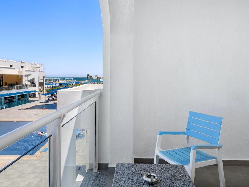 Balkon mit blauem Stuhl, Glasgeländer und Blick auf Hafen bei klarem Himmel.