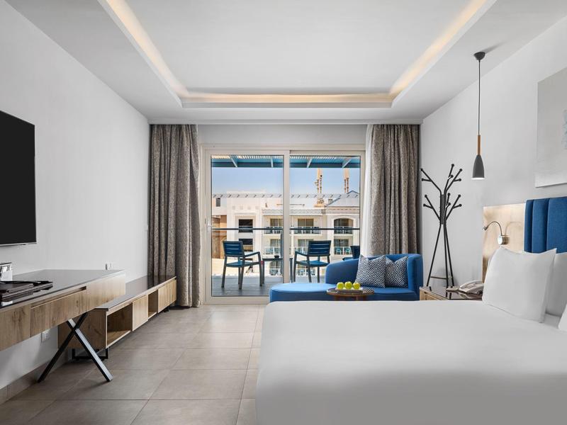 Modernes Hotelzimmer mit großem Bett, blauer Couch, Balkon und Wohnzimmermöbeln.