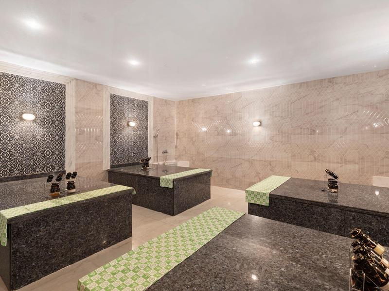 Ein heller Wellnessraum mit dunklen Marmorliegen und beige-grünem Bodenmuster.