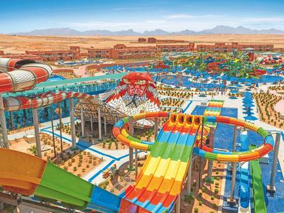 Großer Wasserpark mit bunten Rutschen und vielen Becken in einer sonnigen Wüstenlandschaft.