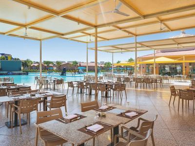 Offener Speisesaal mit mehreren Tischen und Blick auf einen Pool in einer Hotelanlage.