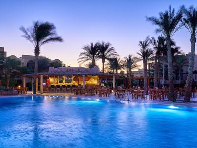 Beleuchteter Poolbereich mit Palmen und Lounge-Bereich bei Sonnenuntergang in einem Resort.