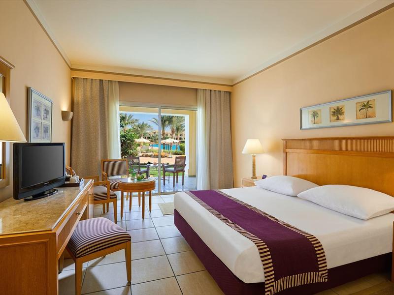 Helles Hotelzimmer mit Doppelbett, Balkon, Holzmöbeln und türkisfarbenem Meerblick.