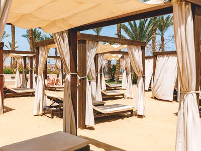 Lettini da lounge ombreggiati sulla spiaggia sabbiosa con palme e cielo blu sullo sfondo.