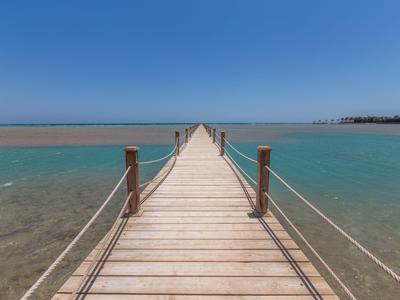 Un lungo molo di legno si estende su acqua calma turchese sotto un cielo azzurro limpido.