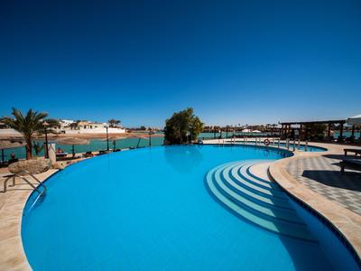 Grande piscina dell'hotel con bordo curvo e scalini, circondata da lettini e palme.