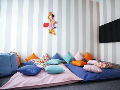 Gemütliche Sitzecke mit bunten Kissen, weichen Decken und flachem Fernseher an gestreifter Wand.